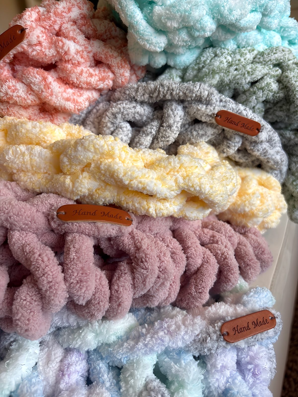 Close-up of two baby blankets in dusty teal and soft lavender, each with a Hand Made leather tag.