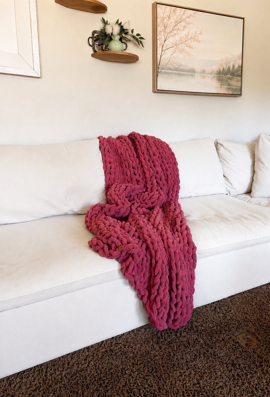 A handmade rose-pink chunky blanket draped over a white sofa.