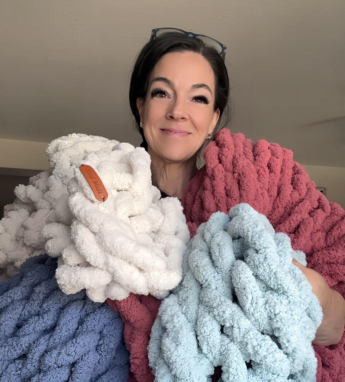 Jenn holding a stack of handmade blankets in cream, dusty rose, soft blue and pale blue.
