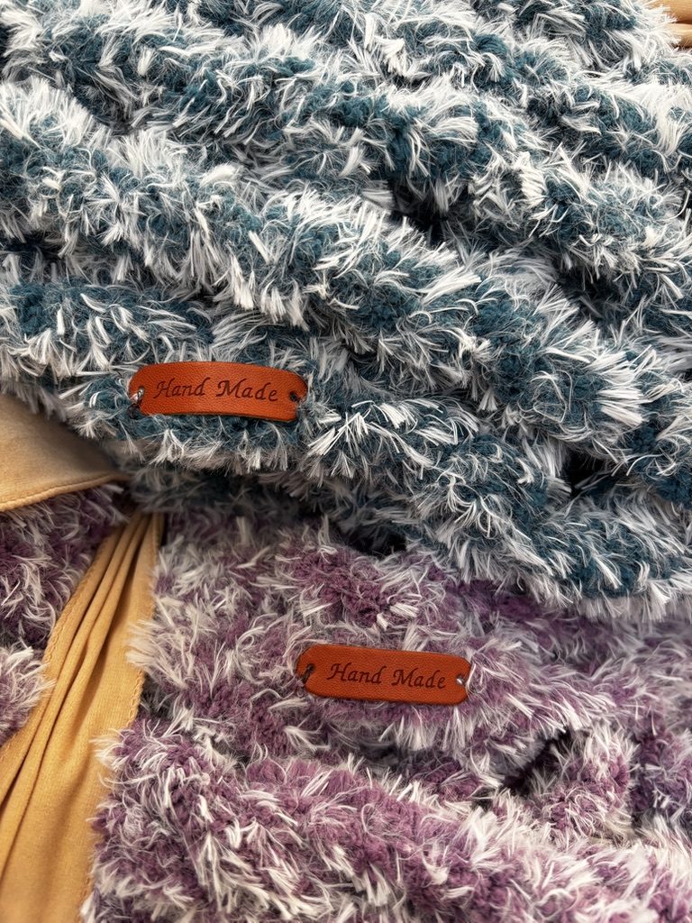 Detail of a leather Hand Made tag stitched onto a teal-and-cream chunky blanket.